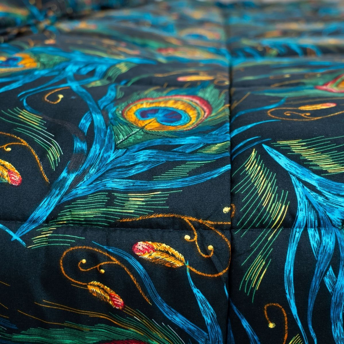 Gros plan sur le tissu matelassé Zelesta Wonderbed Light - Plumes de Paon, qui présente un motif vibrant de plumes de paon en bleu, vert, or et orange - idéal pour un édredon léger d'été ou de printemps (couette légère / couette été).