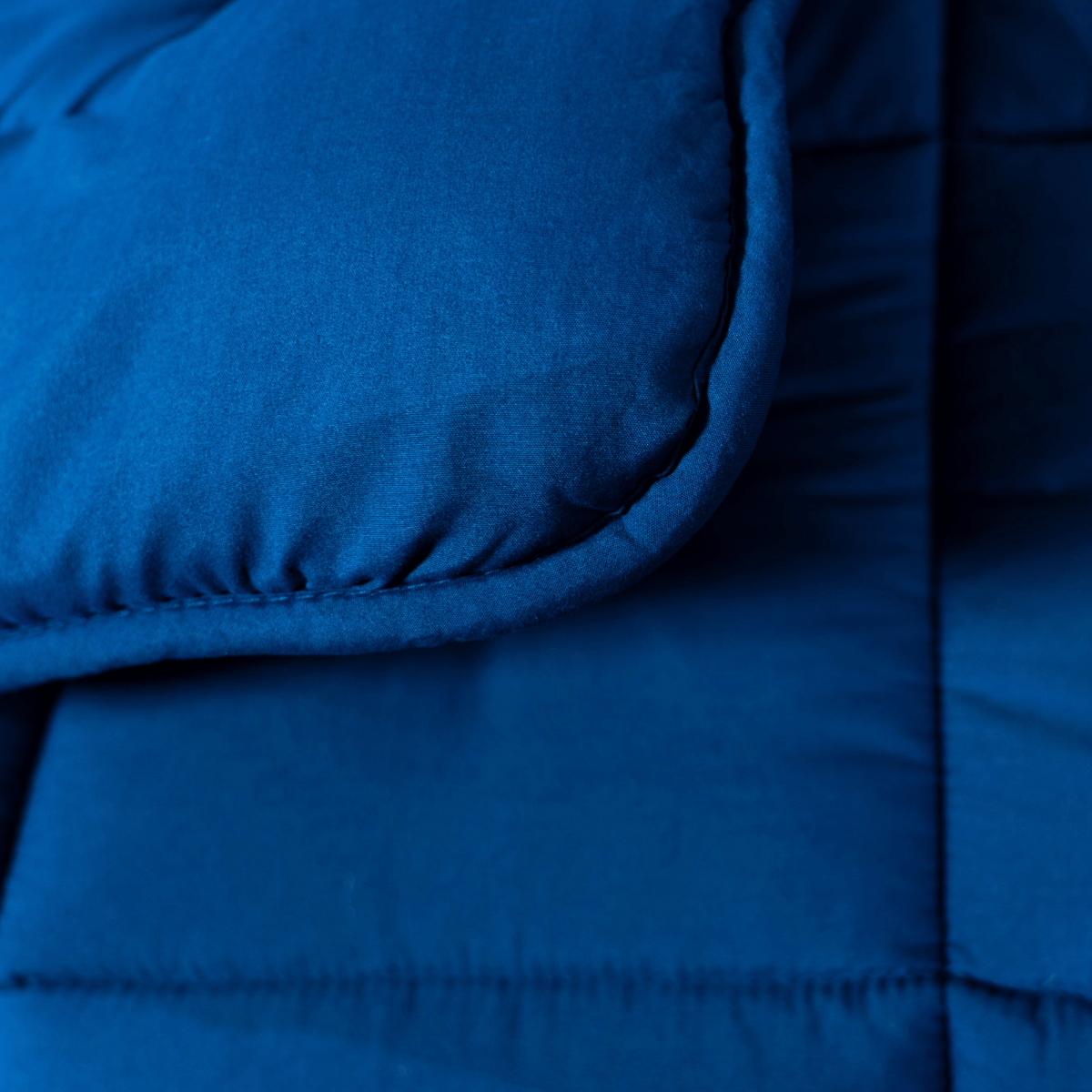 Gros plan sur le lit magique Zelesta - Marine, mettant en valeur son tissu matelassé bleu avec des coutures visibles et un coin soigneusement plié.