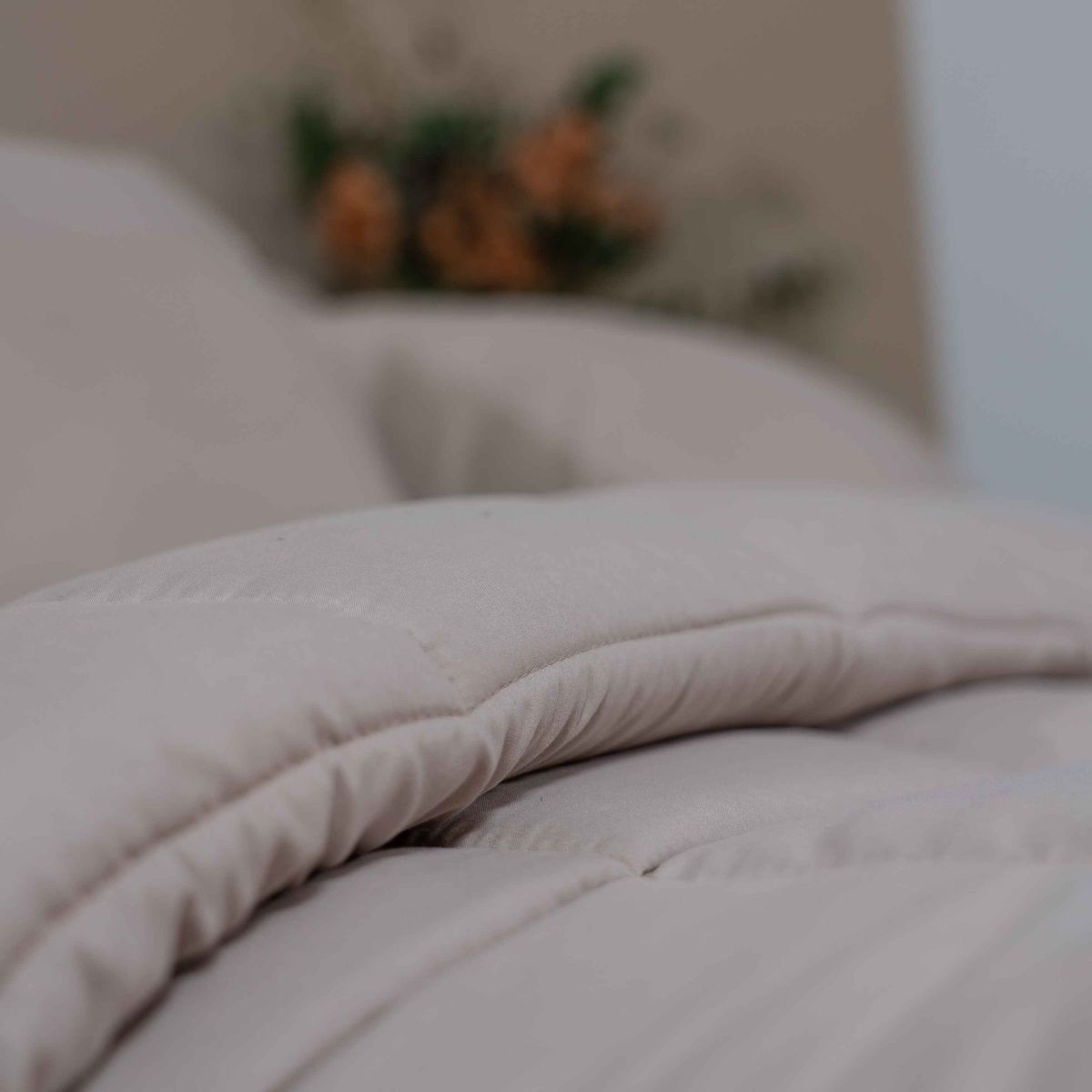 Gros plan d'un lit Zelesta Wonderbed - Taupe plié sur un lit, avec des fleurs et des oreillers flous en arrière-plan.