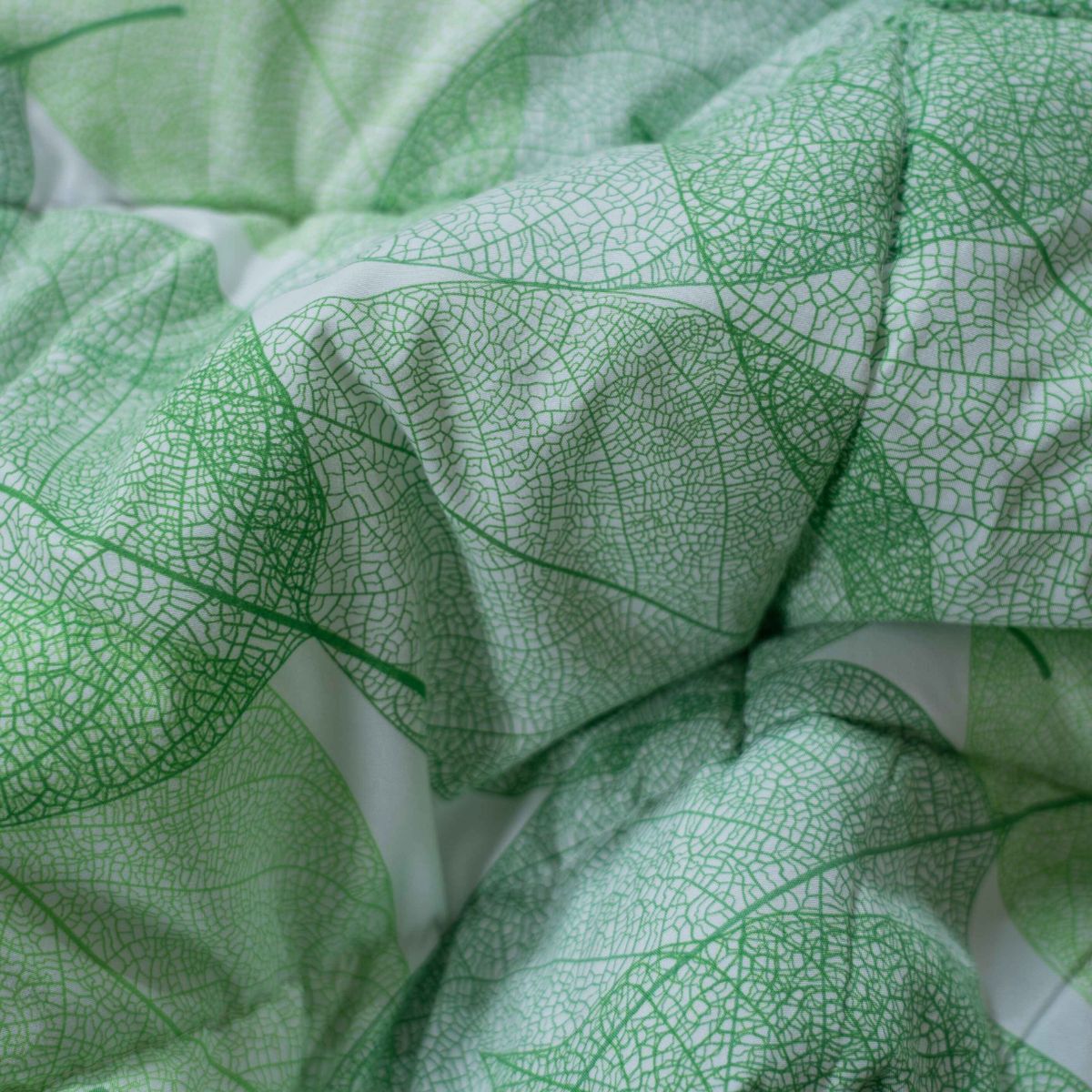 Gros plan sur le tissu Zelesta Wonderbed Light - Feuilles Délicates en microfibre thermorégulatrice, montrant son motif complexe de nervures de feuilles vertes et sa surface texturée et pliée, idéale pour une couette d'été fraîche.