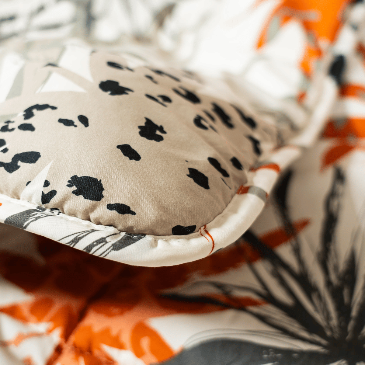 Gros plan sur un oreiller beige avec des taches noires et grises, placé sur le lit Zelesta Wonderbed 4 Saisons Double - Jungle Orange, mettant en valeur son motif botanique orange, gris et blanc pour un confort optimal.