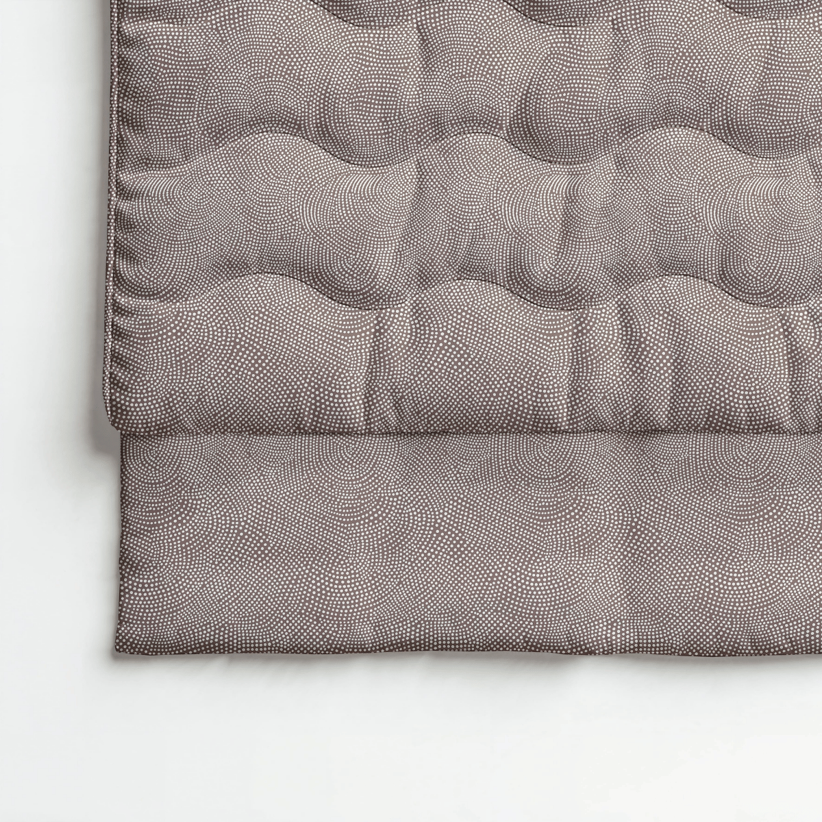 Gros plan sur le Zelesta Royalbed Coton - Marron Fauve, une couette anti-allergique matelassée pliée avec un subtil motif circulaire en pointillés dans des tons sourds, présentée sur une surface blanche.