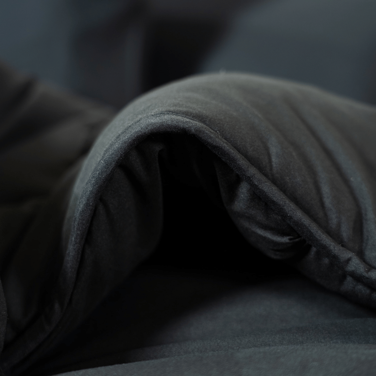 Gros plan sur le lit magique Zelesta - Noir, plié avec un tissu rembourré et anallergique, une texture douce et des bords incurvés sur un fond sombre.