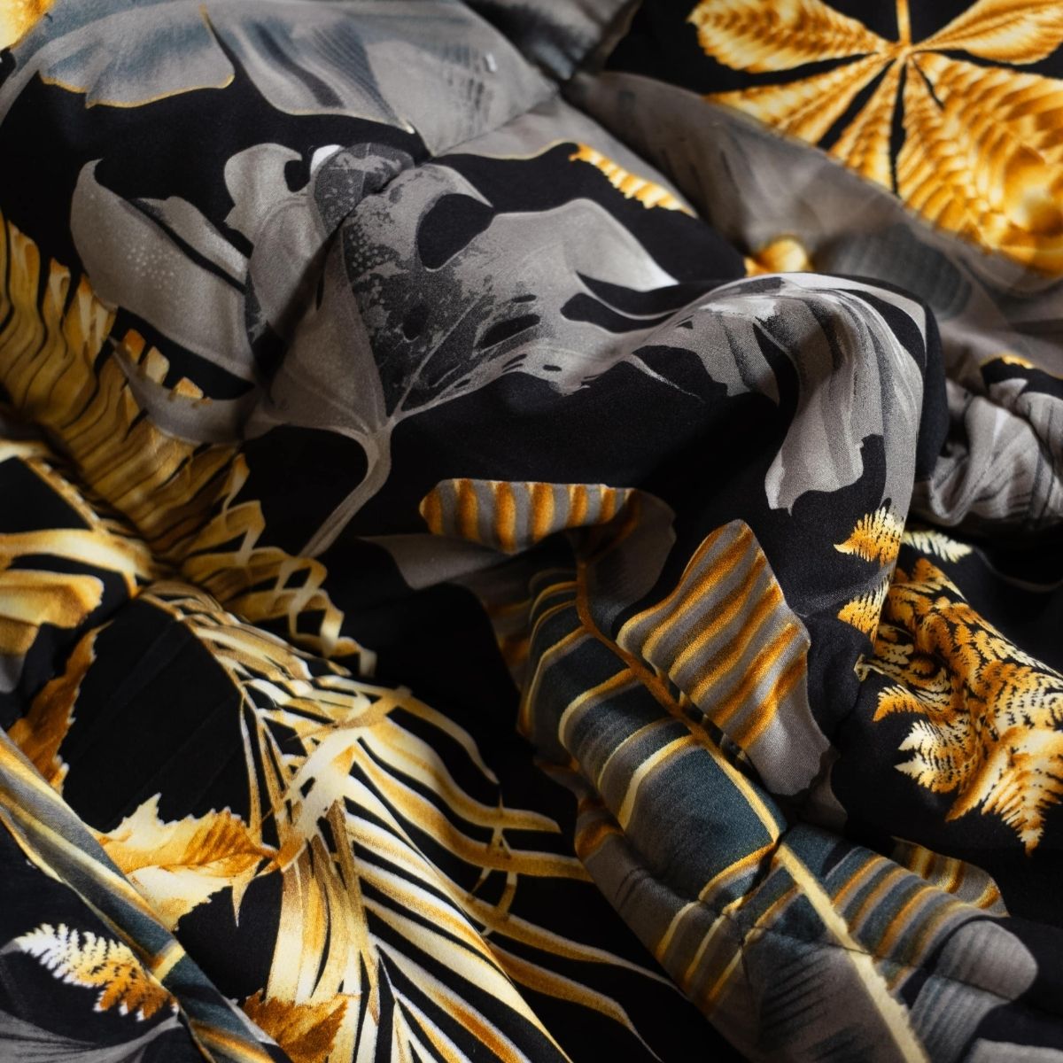 Gros plan d'un tissu froissé présentant un motif de feuilles tropicales noires, jaunes et grises de la couette d'été en microfibre hypoallergénique Zelesta Wonderbed Light - Feuilles Dorées.