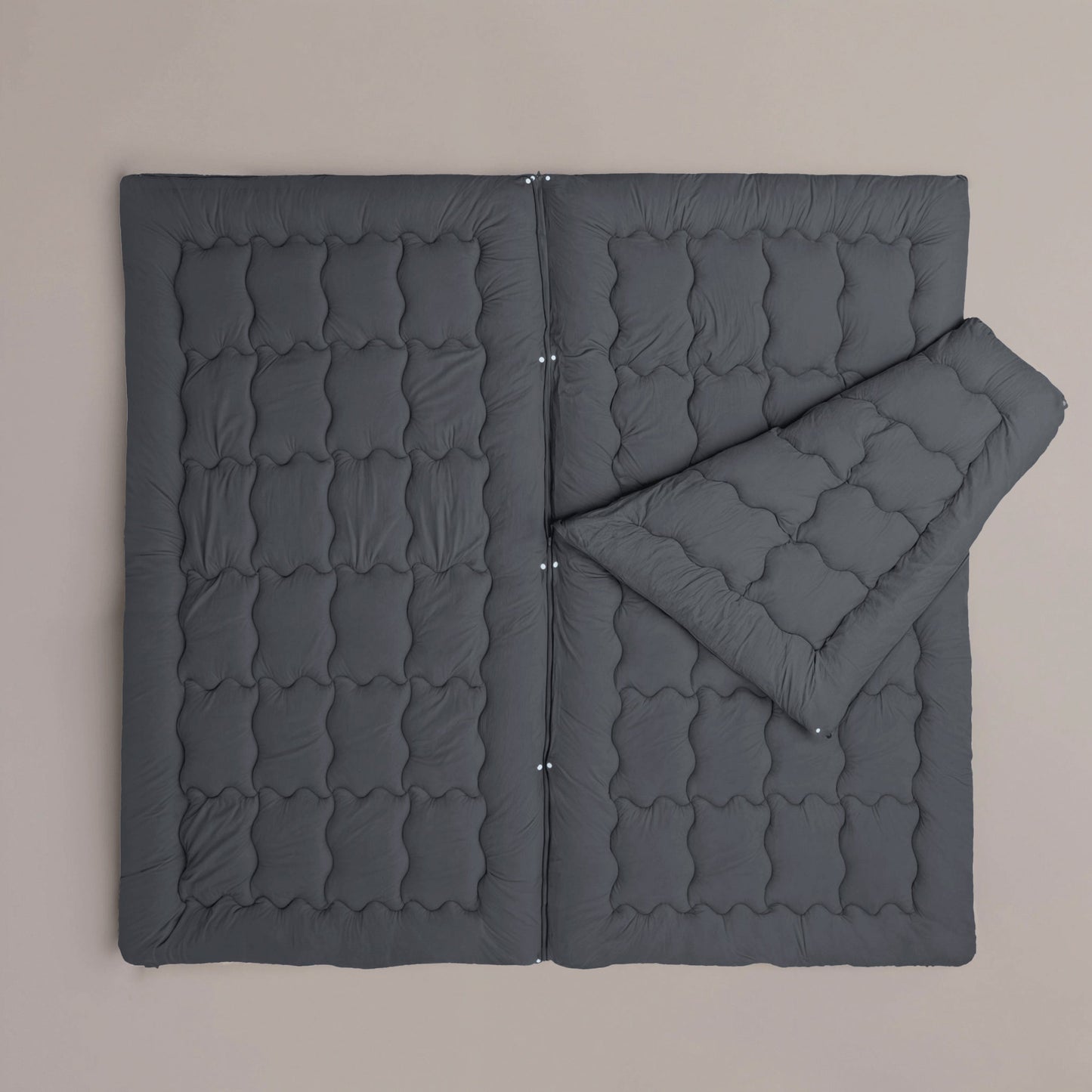 La couette Zelesta Flexibed - Anthracite, une couette piquée toutes saisons gris foncé, est présentée à plat sur un fond neutre, avec un coin replié pour mettre en valeur son épaisseur et sa texture.