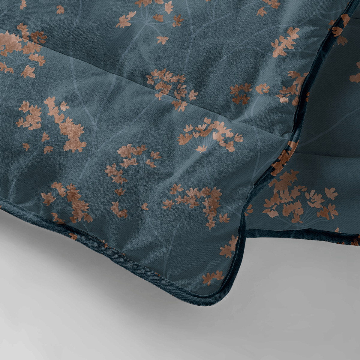 La couette Zelesta Royalbed - Majestic est une couette thermorégulatrice bleu foncé présentant un subtil motif de branches avec des feuilles de cuivre, partiellement pliée sur une surface gris clair.