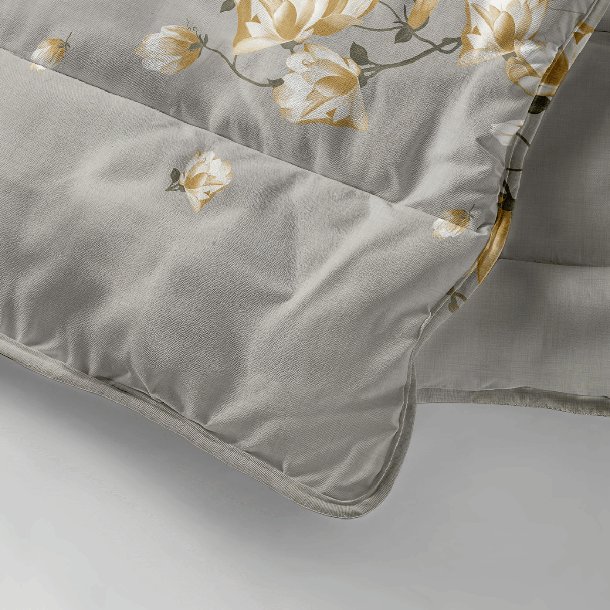 Gros plan sur la Zelesta Royalbed - Fleur Blanche, une couette grise lavable en machine avec un motif floral jaune et blanc, présentant des coutures piquées et une texture de tissu douce.