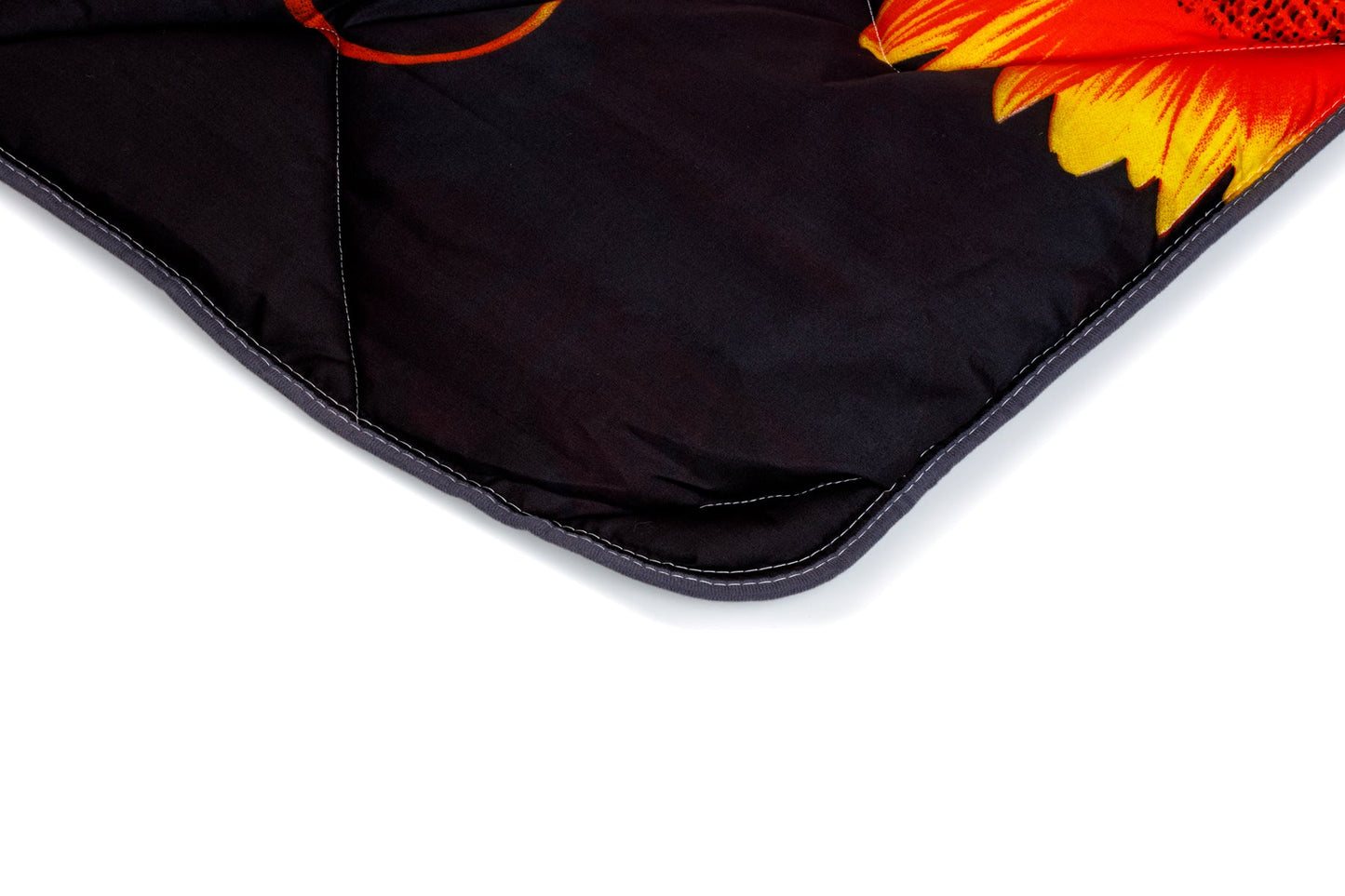 Gros plan sur le coin d'un lit Zelesta Wonderbed Light - Fleurs d'Été, composé d'un tissu microfibre hypoallergénique noir avec coutures apparentes et d'un motif floral partiel jaune et rouge sur fond blanc.