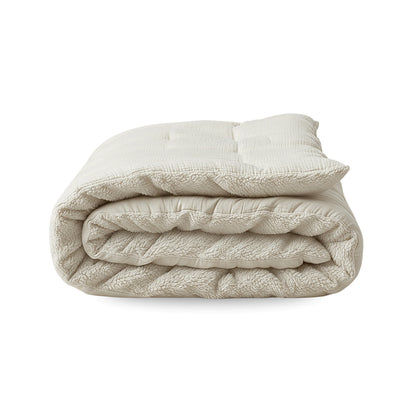 La couverture matelassée Zelesta Teddy Mousseline de Coton - Beige est soigneusement pliée et présentée sur un fond blanc.