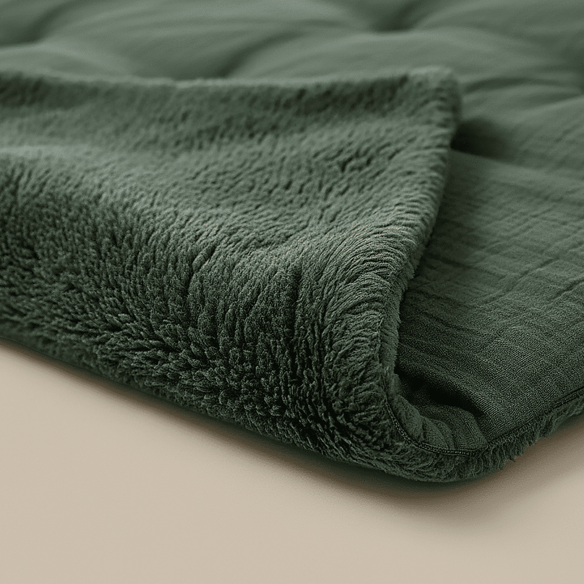 Gros plan sur la couverture Zelesta Teddy Mousseline de Coton - Vert, une couverture texturée en peluche vert foncé avec une surface douce et duveteuse et un dessous matelassé, présentée sur un fond beige.