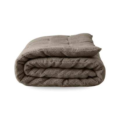 La couverture Zelesta Teddy Mousseline de Coton en taupe, au design matelassé et au tissu mousseline de coton doux, est présentée pliée sur un fond blanc uni.